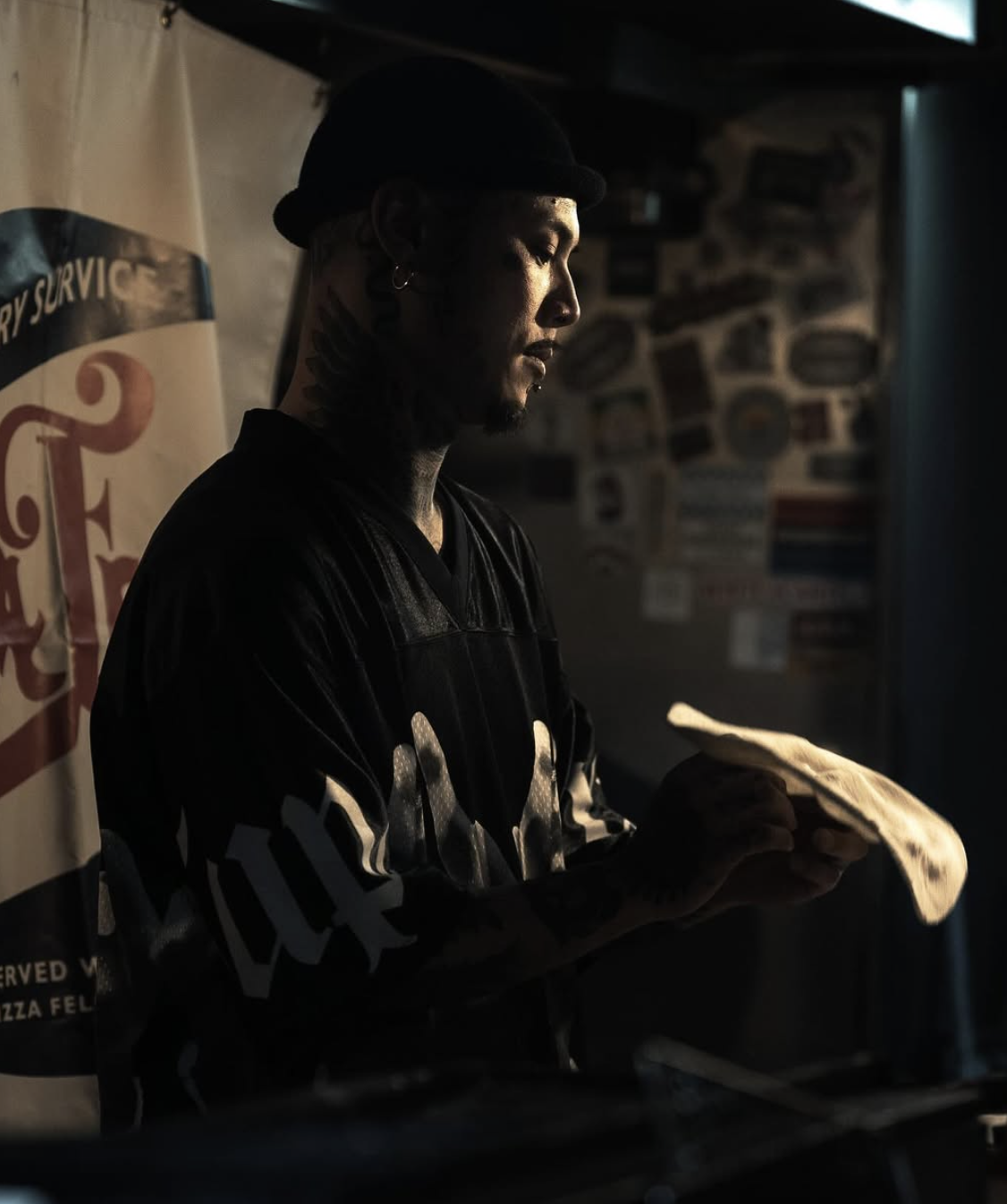 暗い店内でピザ生地を扱うTAKUMA PIZZA